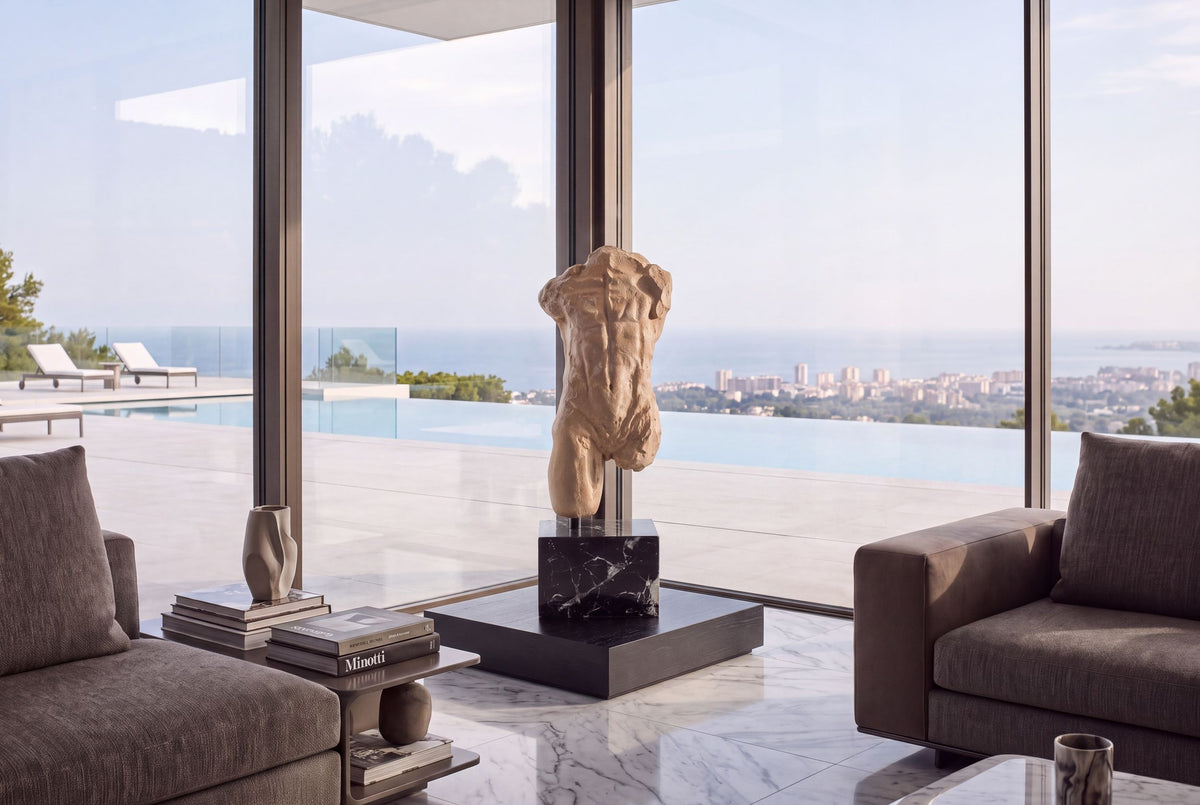 Headless bronze torso sculpture by a sea-view window